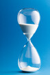 Close up of hourglass with white sand and copy space on blue background
