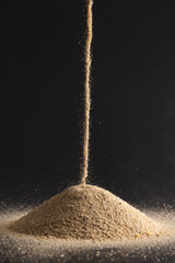 Wall Mural - close up of sand pouring into heap and copy space on black background