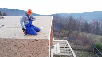 Wall Mural - Carpenter hammering nail into OSB panel on the roof top of future cottage. Man worker building wooden frame house. Carpentry and construction concept.