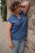 © Вероника Зеленина - A beautiful girl is wearing a blue t-shirt and jeans, the overweight woman posing against stone biege wall. The fashion outfit for plus-size woman for the city, minimalizm urban style clothes