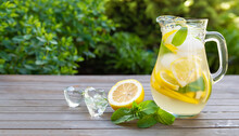 Lemonade Pitcher With Lemon, Mint And Ice On Garden Table. View With Copy Space
