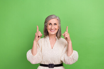 Sticker - Photo portrait of beautiful grandma fingers point look up empty space wear trendy white outfit isolated on green color background