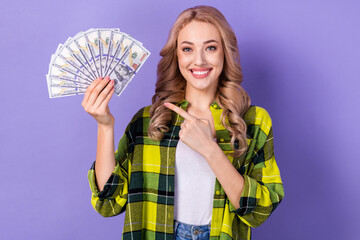 Poster - Photo of gorgeous successful lady beaming smile direct finger arm hold dollar bills isolated on violet color background