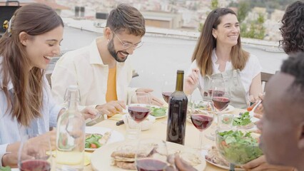 Wall Mural - Multiethnic friends having fun at rooftop bbq dinner party - Group of young people diner together sitting at restaurant dining table - Cheerful multiracial teens eating food and drinking wine outside	