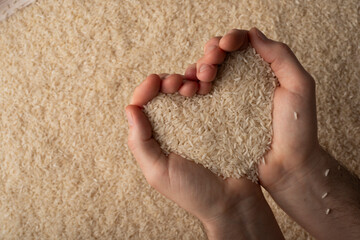 Wall Mural - Human hands in shape of heart holding handful of rice on rice background