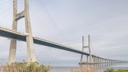 Wall Mural - Architectural landmark Vasco da Gama Bridge over the Tagus River in Lisbon, Portugal. Green grass and cloudy sky. The longest bridge in the European Union.