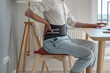 © DimaBerlin - Man freelancer works types on computer keyboard wearing back support belt corset on lower back during exacerbation to treatment of hernia. Back pain health problems as consequences of sedentary work.