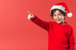 © raquel - Little kid with christmas hat pointing to blank space on red background. Generative AI