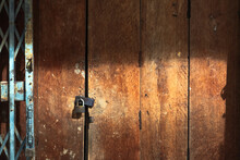 Old Gold Steel Lock And Damaged And Rusted Steel Door On Wooden Door. Locked On Wooden Door With Old Steel Metal Shutter And Folding Door Gate. Old Wooden Door With Locked Key. Vintage Background.