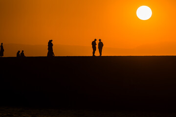 Wall Mural - Silhouette of tourists watching the sun set behind a distant mountain in summer