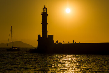 Wall Mural - Silhouette of a lighthouse and small yacht during a beautiful golden sunset on a Greek island in summer