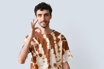 Wall Mural - Handsome man in tie-dye t-shirt showing OK on light background