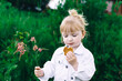 © Анна Молько - a very cute blonde girl in a white jacket is holding a pink flower and eating cookies in the park. happy childhood