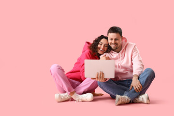Wall Mural - Young couple using laptop on pink background