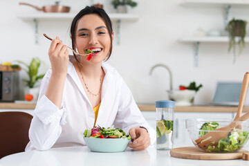 Canvas Print - Young woman eating vegetable salad in kitchen