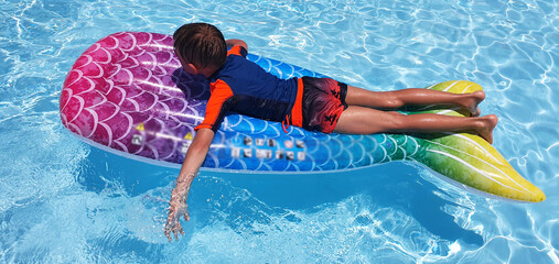 
The child floats on an inflatable mattress in the pool. Summer vacation for a family with children in the water park. A boy floats on an inflatable mattress in a clean swimming pool in a hotel.