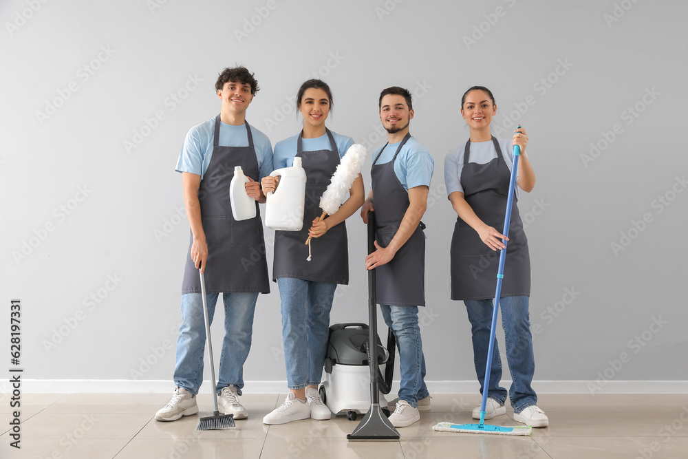 Young janitors with cleaning supplies near grey wall