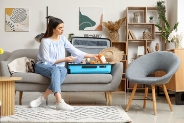 Canvas Print - Young woman packing sunscreen cream in suitcase at home