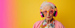 Leinwandbild Motiv Studio portrait of eccentric elderly woman listening to music on headphones, colorful pink and yellow background
