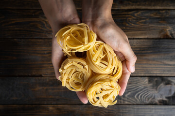 Raw uncooked Italian pasta tagliatelle held in two hands over a dark wooden background