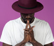 © ADDICTIVE STOCK - Thoughtful young black man standing in hat near purple wall with fingers near lips