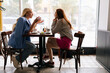 © dikushin - Side view of young redhead woman talking to blonde female friend, spending time together during drinking coffee at cozy restaurant, sitting at table on background of window after long separation.