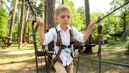 Wall Mural - Portrait of little boy crossing the rope bridge between two trees in park