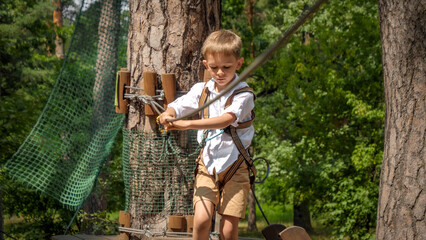 Canvas Print - Portrait of concentrated boy holding safety rope while crossing bridge in outdoor summer camp. Active childhood, healthy lifestyle, kids playing outdoors, children in nature.