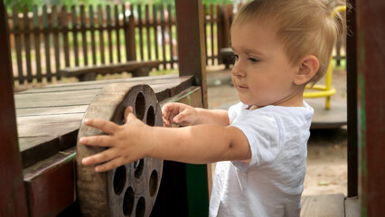 Portrait of adorable toddler boy playing in wooden car in park and holding steering wheel