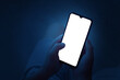 A teenager holds a smartphone with two hands at night. Phone with white screen on defocused dark blue background. There is a work path in the file.