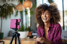 Beautiful Smiling Woman Blogger Making A Video For Her Blog On Cosmetics Using A Phone With Tripod. Smartphone Standing On Table On Tripod Stabilizer, Recording Female Blogger. Digital Ai