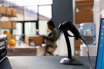 Wall Mural - Selective focus of store scanner standing on counter desk in warehouse, in background african american employee preparing packages for delivery. Stockroom supervisor working at customers online orders