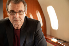 Portrait Of Mature Business Man Wearing Glasses Sitting In Seat Aboard Private Jet 