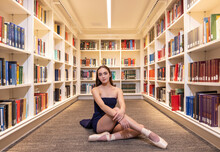 Portrait Of Young Female Ballerina Sitting On Floor Of Library Pulling Looking To Camera 