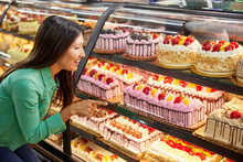 Female Customer Looking Through Display Case And Choosing Cake From Bakery Counter In Grocery Store