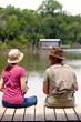 © SuperStock - Older couple sitting on edge of covered boat dock , woman with fishing line in the water