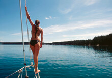 Young Woman Standing On Bow Railing Of Boat In Calm Water 