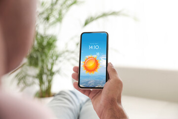 man checking weather using app on smartphone at home, closeup. data and illustration of sun on scree