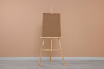 Wall Mural - Wooden easel with blank board near beige wall indoors