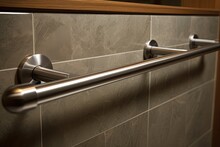 A detailed picture of a stainless steel grab bar handrail affixed to a wall covered in gray stone tiles can be seen in a bathroom designed for individuals with disabilities in a hotel setting.