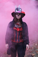 Wall Mural - A woman in the guise of Baron Sabbath poses in red smoke. The model is dressed in a corset, a cardigan and a top hat decorated with skeleton figures. Model looking at the camera