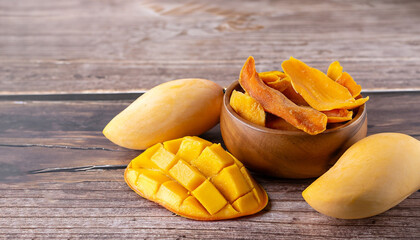 Poster - Dried mango in wooden bowl and fresh mango fruit on wood textured background. Copy space. Superfood, vegan, vegetarian food concept. Macro of orange dried mango slices, selective focus. Healthy snack.