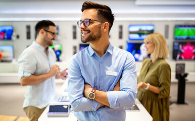 Happy seller man helping to people to buy a new digital smart devices in tech store.