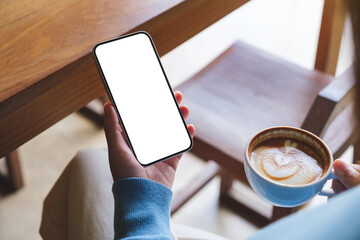 mockup image of a woman holding mobile phone with blank desktop screen and coffee cup