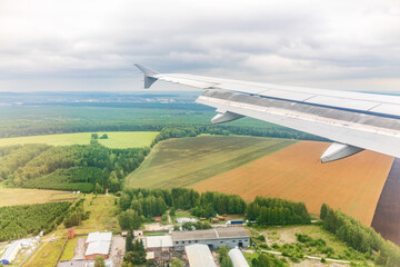 View of airplane wing, blue skies and green land during landing. Airplane window view.