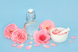 Rose flower perfume in heart shaped bottle with flowers and loose petals on blue. Preparation of scented floral product, gift for Valentines Day, birthday, anniversary or Mothers day.
