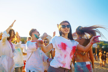 Cheerful young friends with colorful paint on clothes and bodies have fun together at holi festival. Beach party. Friendship, rest, holidays.