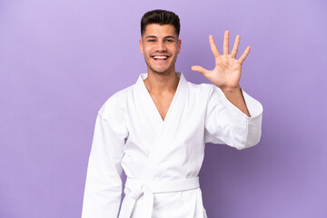 Wall Mural - Young caucasian man doing karate isolated on purple background counting five with fingers