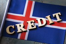 Text From Wooden Letters And Flag On Abstract Background, Concept On The Theme Of The Debt Burden Of The People Of Iceland
