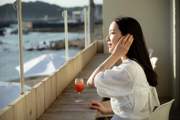 Beautiful Asian woman drinking a cocktail on the terrace of a cafe overlooking the sea